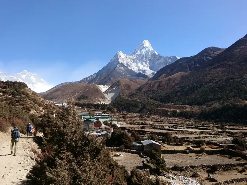 Eine Wandergruppe auf einem Pfad im Khumbu-Tal in Nepal mit Blick auf den schneebedeckten Gipfel der Ama Dablam.