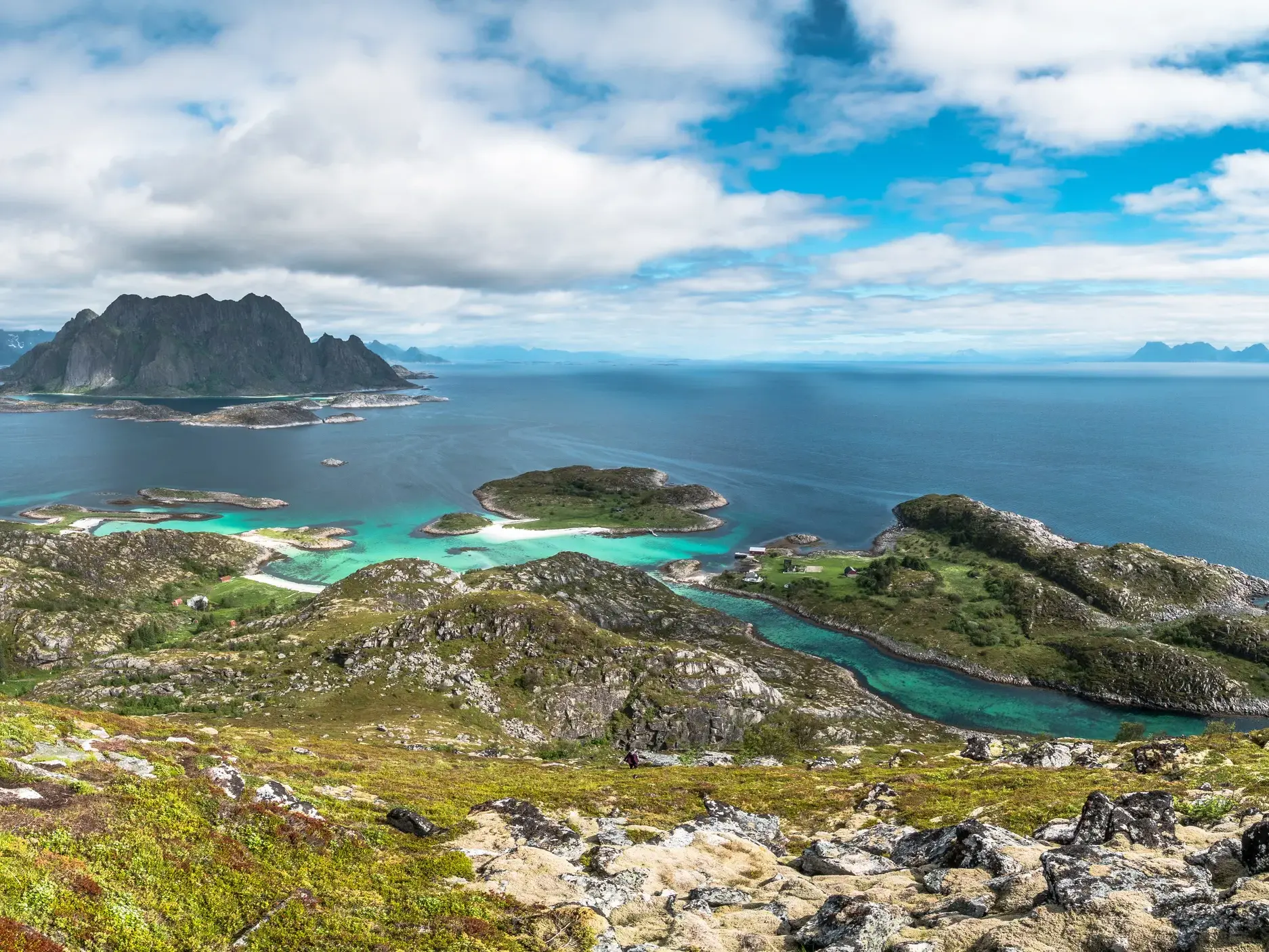 Panoramablick von einem Gipfel auf die zerklüftete Schärenwelt der Lofoten mit türkisem Wasser und schroffen Bergen.