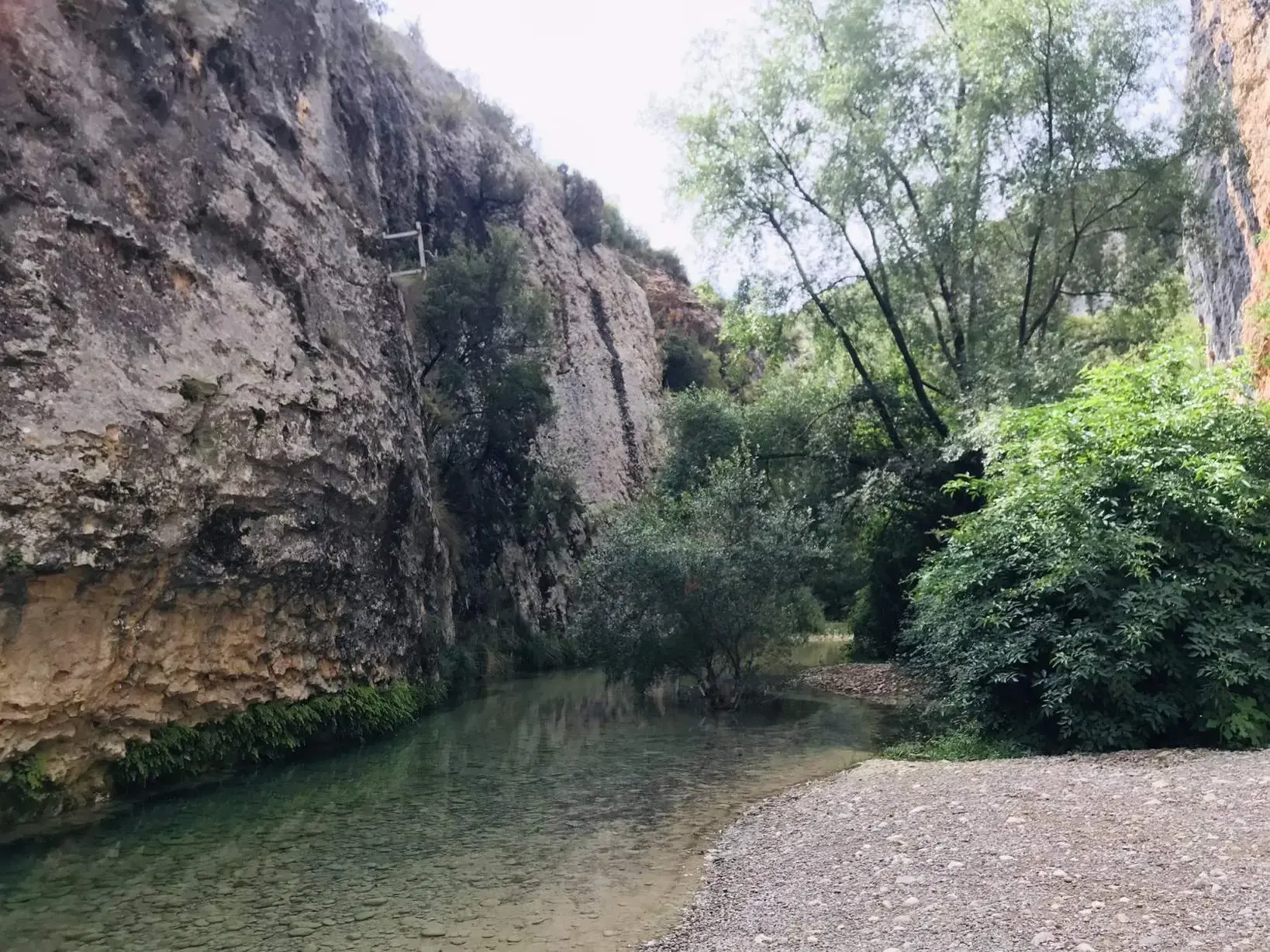Glasklarer Río Verde in einer Felsenschlucht der Sierra de Guara mit einem Kiesufer und üppig grünen Bäumen in Aragonien.