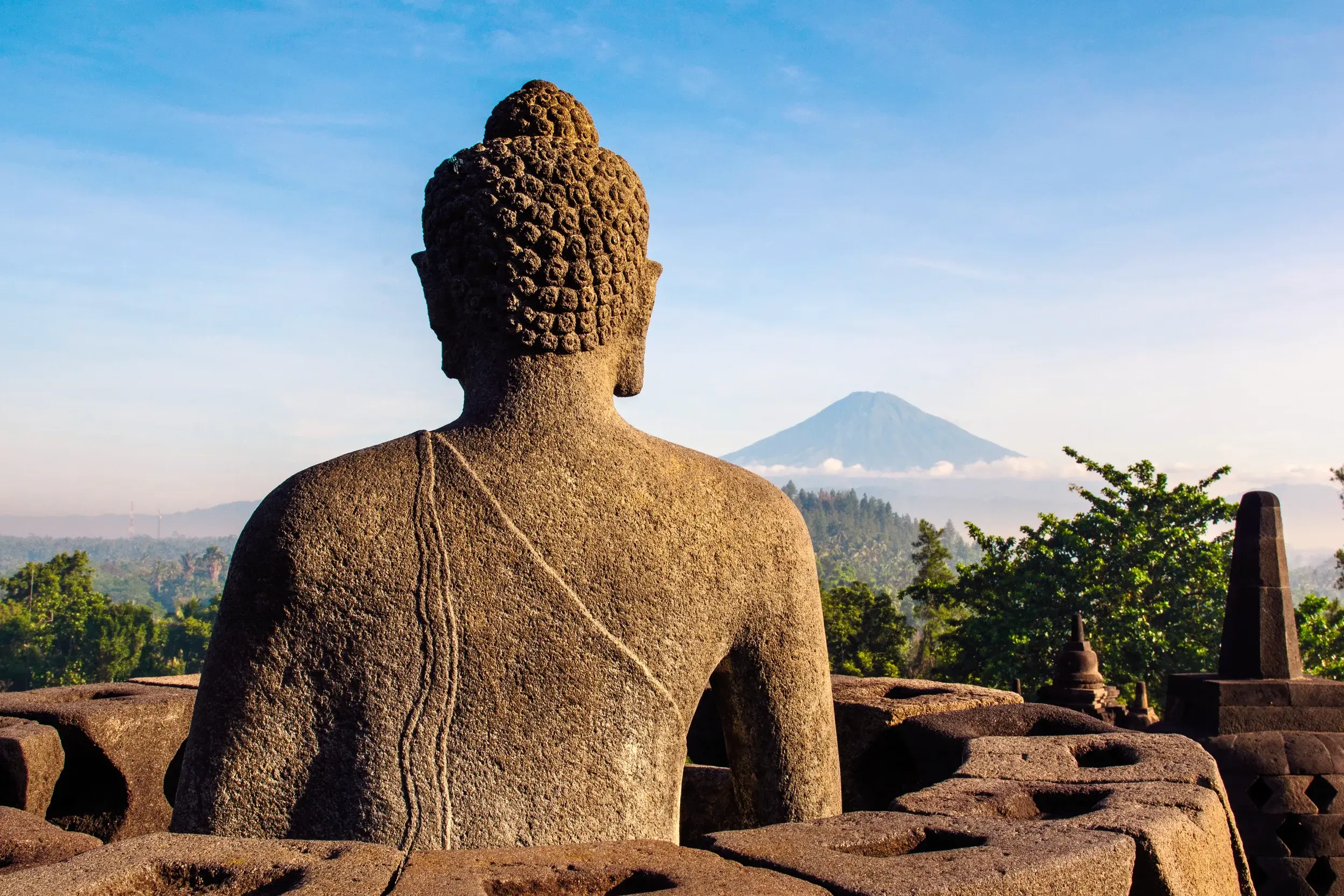 Blick von der buddhistischen Tempelanlage BOROBUDUR über eine Buddha-Statue hinweg auf einen Vulkan im Morgennebel auf Java.
