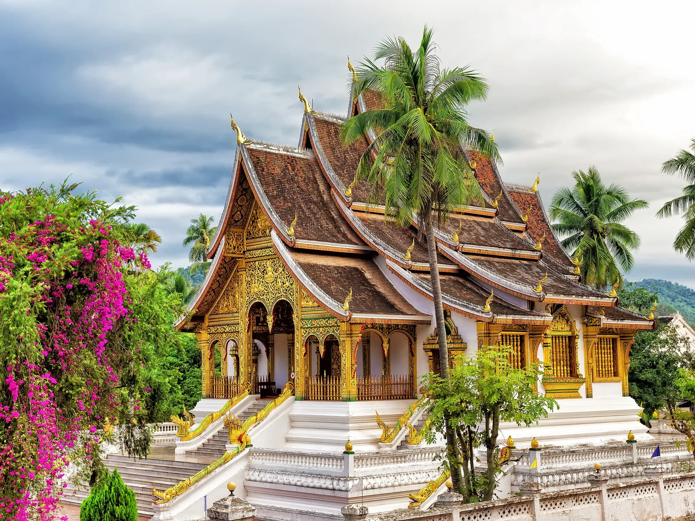 Der goldverzierte Königspalast-Tempel in Luang Prabang, umgeben von Palmen und blühender Bougainvillea.