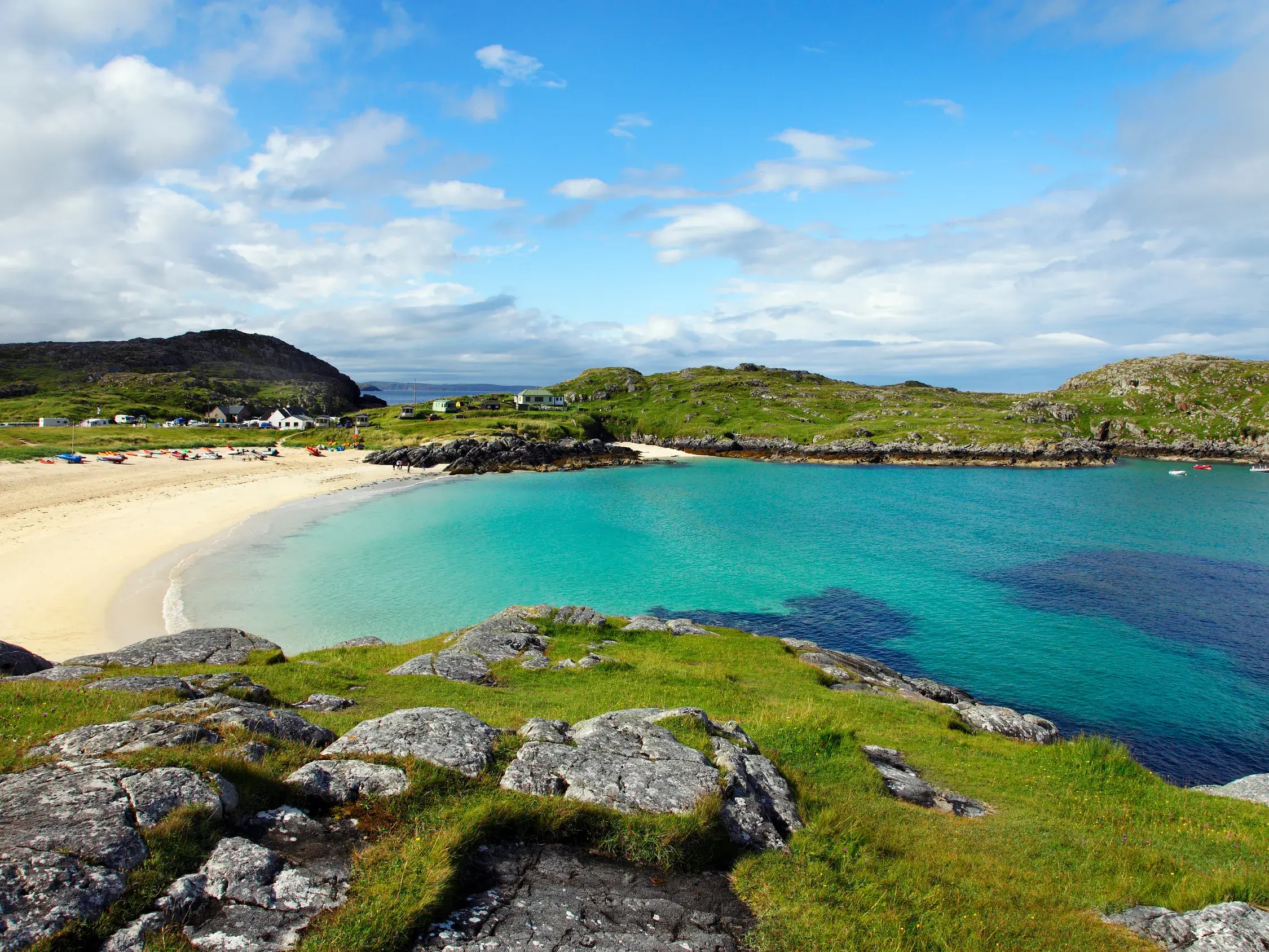 Blick von einem grünen Hügel auf den weißen Sandstrand und das türkisfarbene Wasser des malerischen Achmelvich Beach in Schottland.