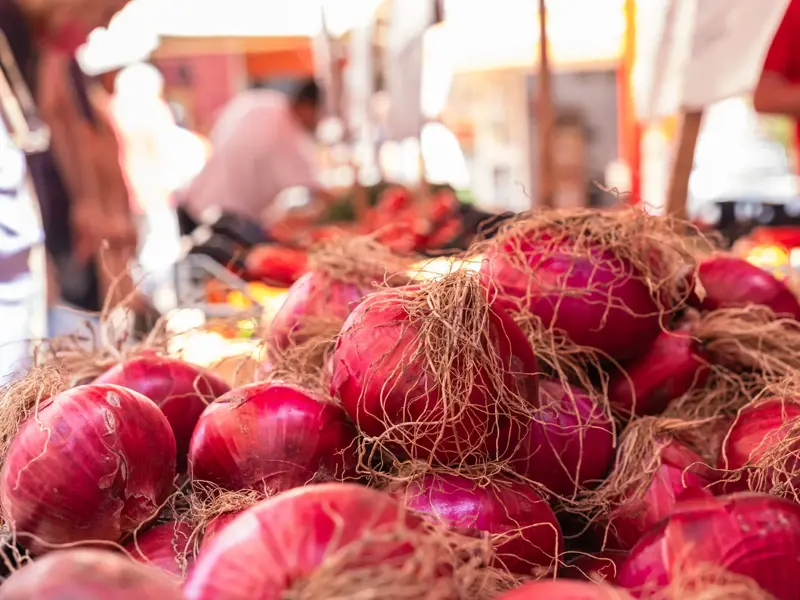 Nahaufnahme von frischen, roten Zwiebeln auf einem belebten Marktstand auf dem Mercato del Capo in Palermo.