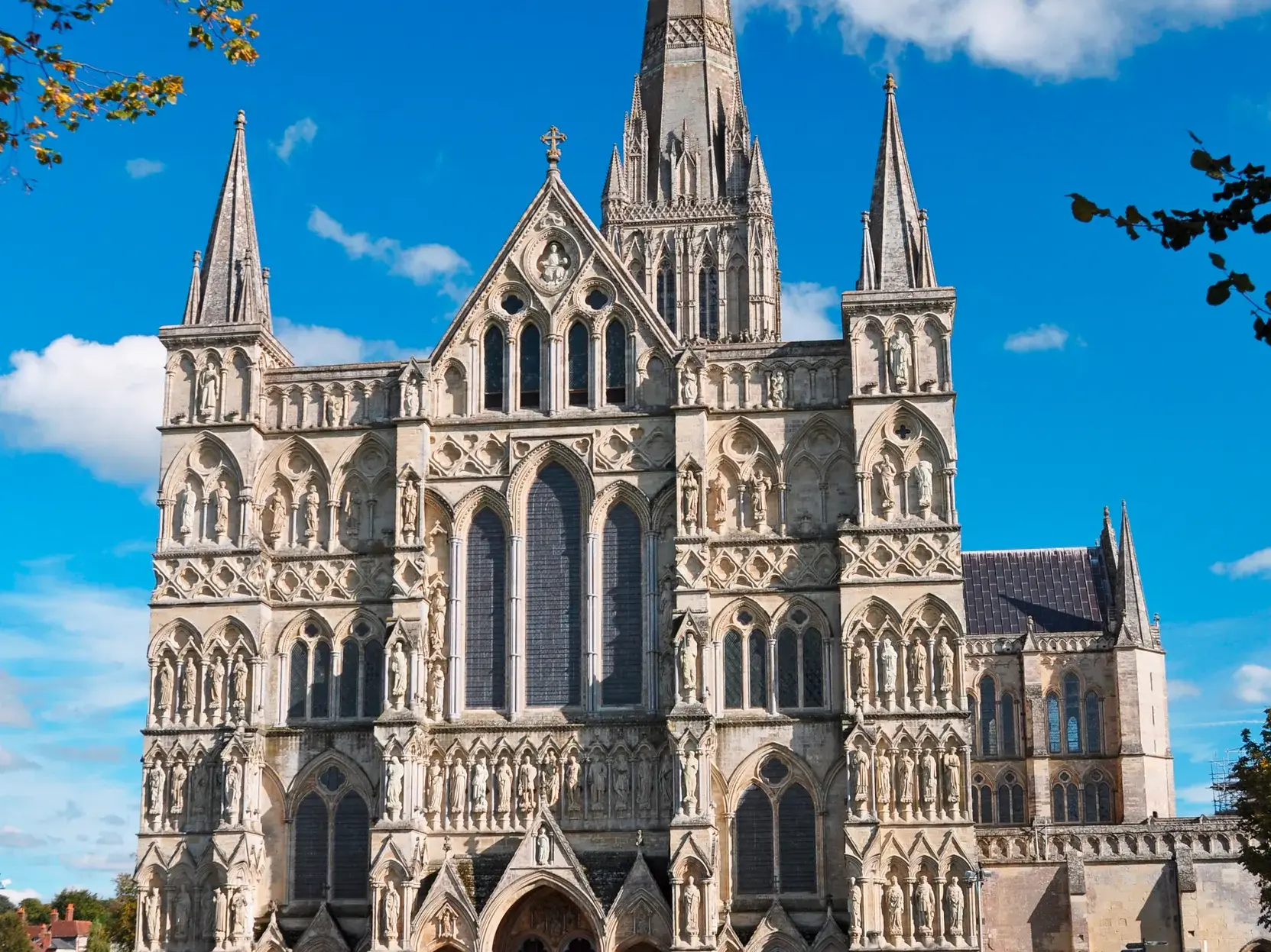 Besucher einer Studienreise spazieren auf einer Wiese vor der imposanten, gotischen Westfassade der Kathedrale von Salisbury.
