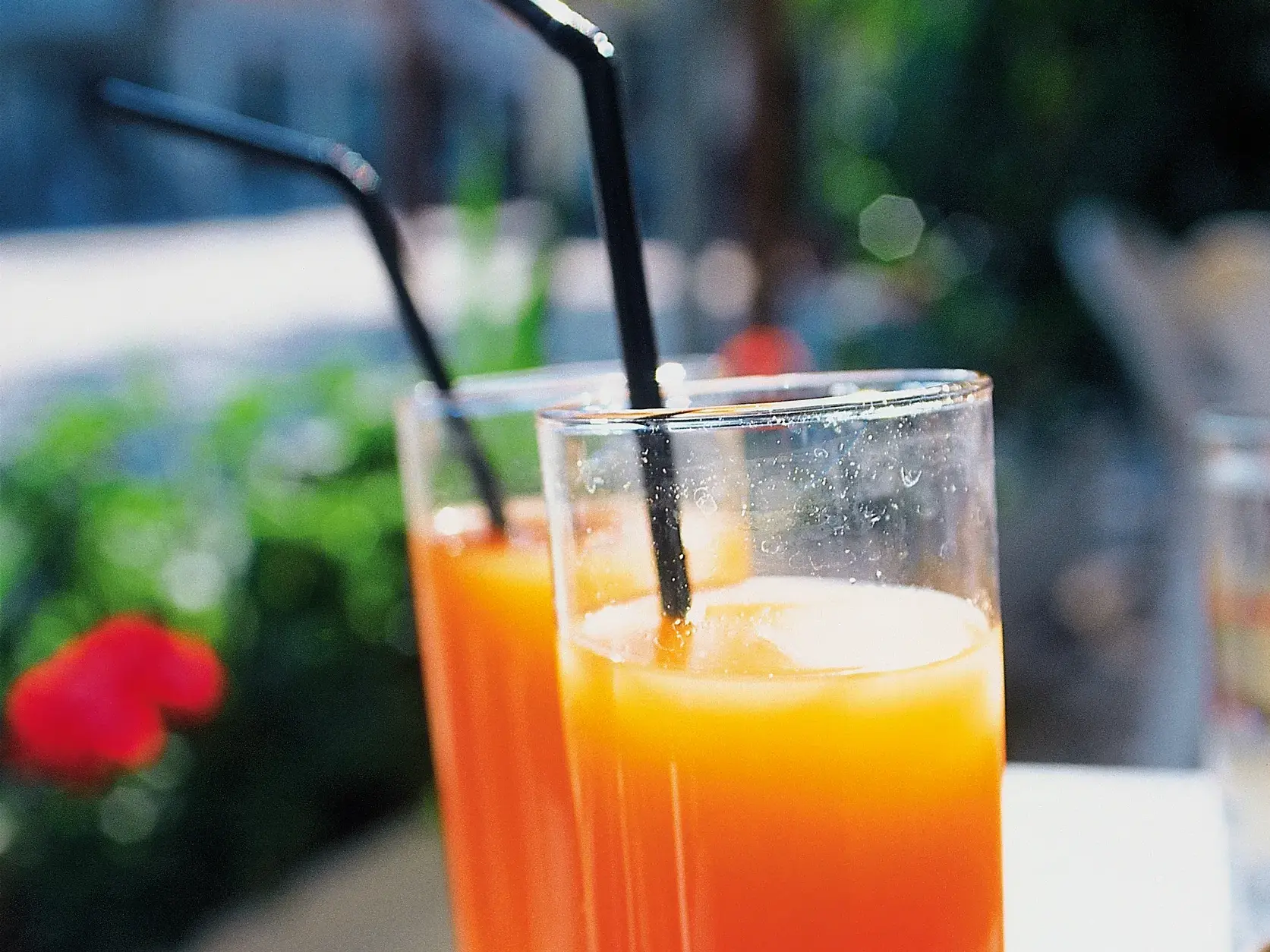 Zwei Gläser mit einem kühlen, orangen Sundowner stehen auf einem Tisch in einer sonnigen Taverne auf den Kykladeninseln.