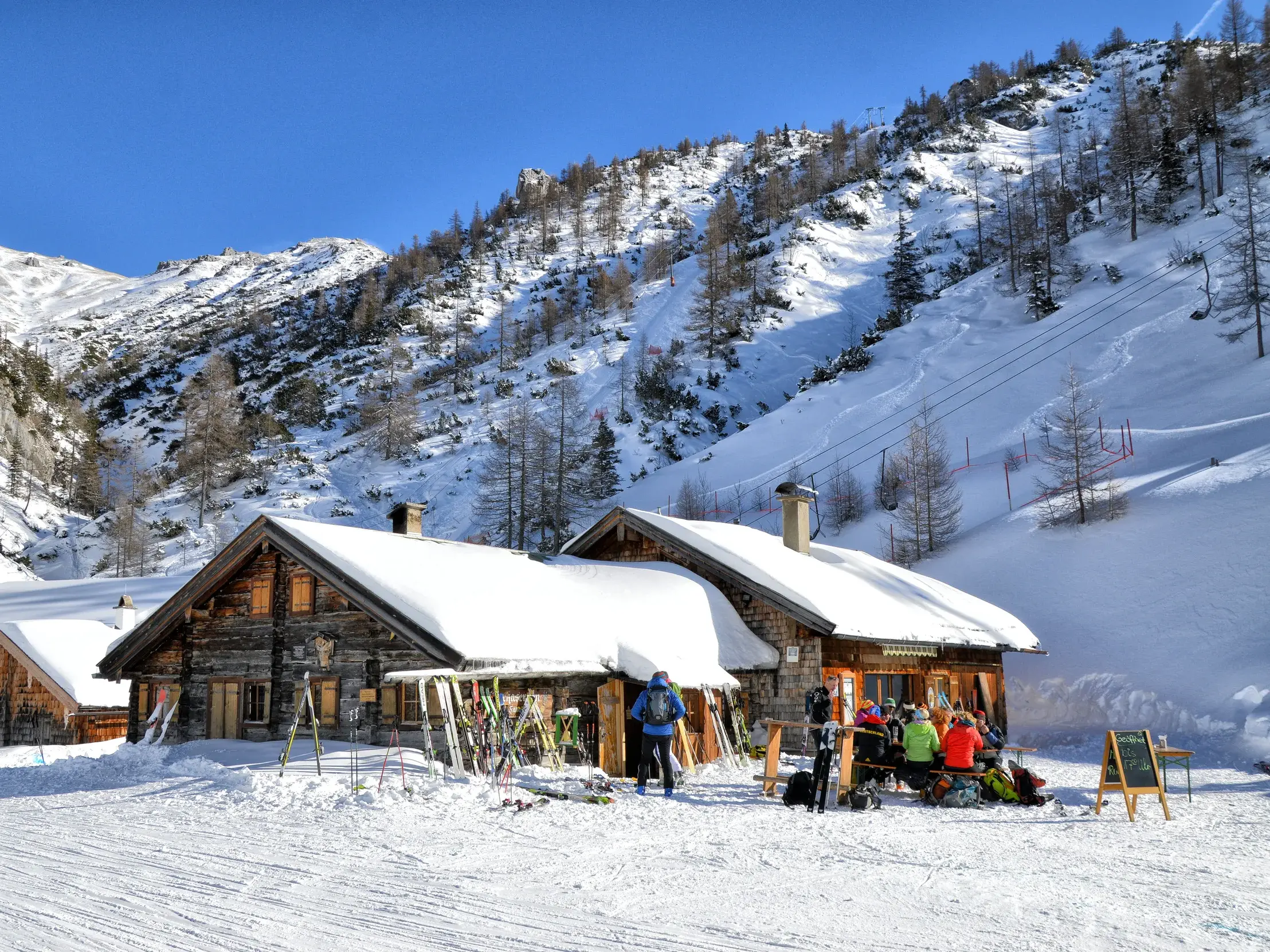 Verschneite Wimbachgrieshütte im Wimbachgries, an der Wanderer bei einer Schneeschuhwanderung eine sonnige Pause einlegen.