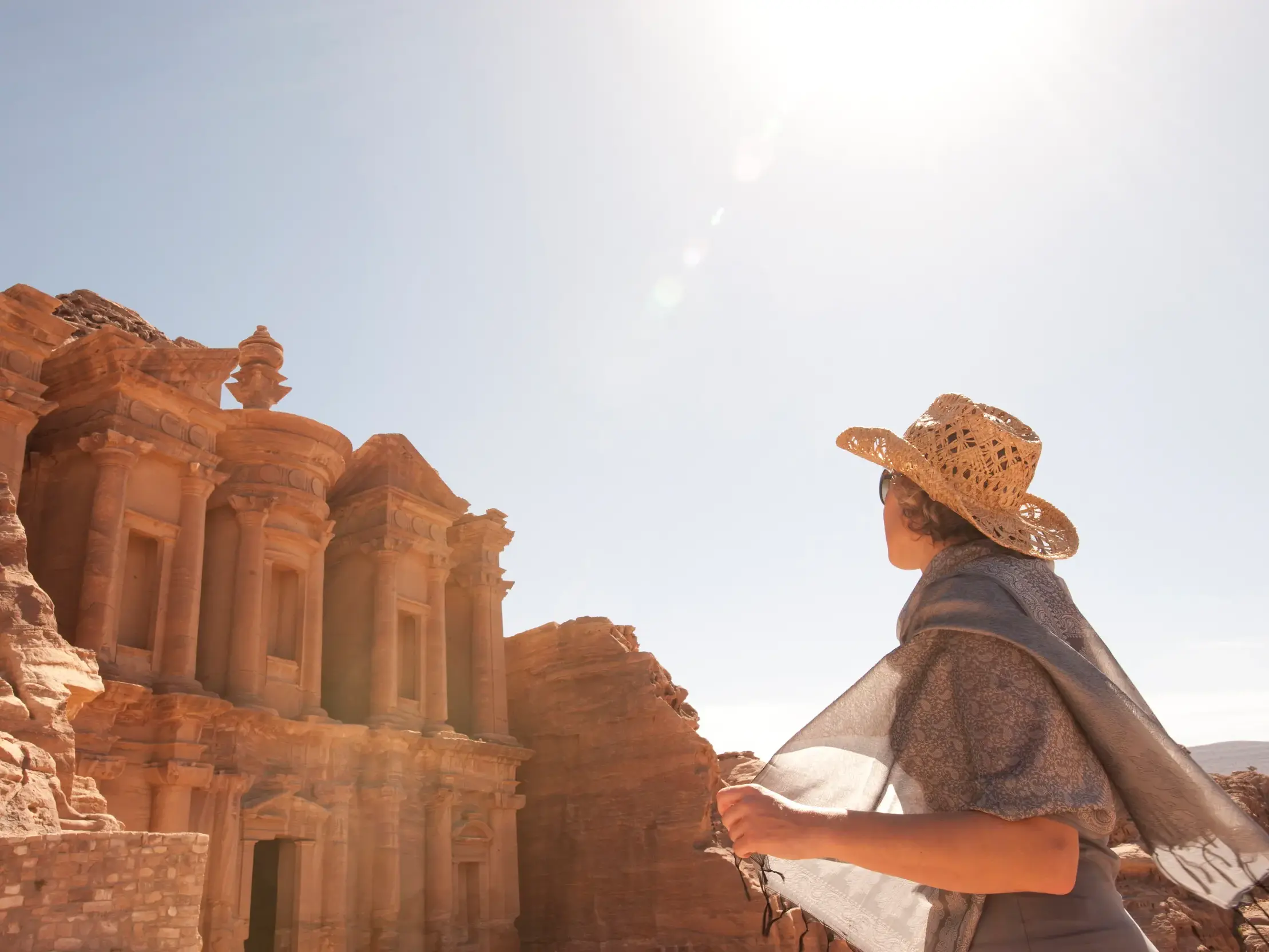 Eine Reisende mit Strohhut bestaunt auf einer Wanderung das in den Fels gehauene Kloster Ed-Deir in Petra, Jordanien.