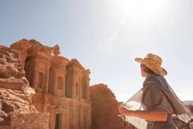 Eine Reisende mit Strohhut bestaunt auf einer Wanderung das in den Fels gehauene Kloster Ed-Deir in Petra, Jordanien.