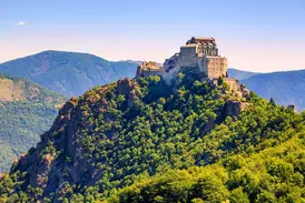 Die Klosteranlage Sacra di San Michele thront bei Sonnenschein auf einem Felsgipfel über dem grünen Susatal im Piemont.