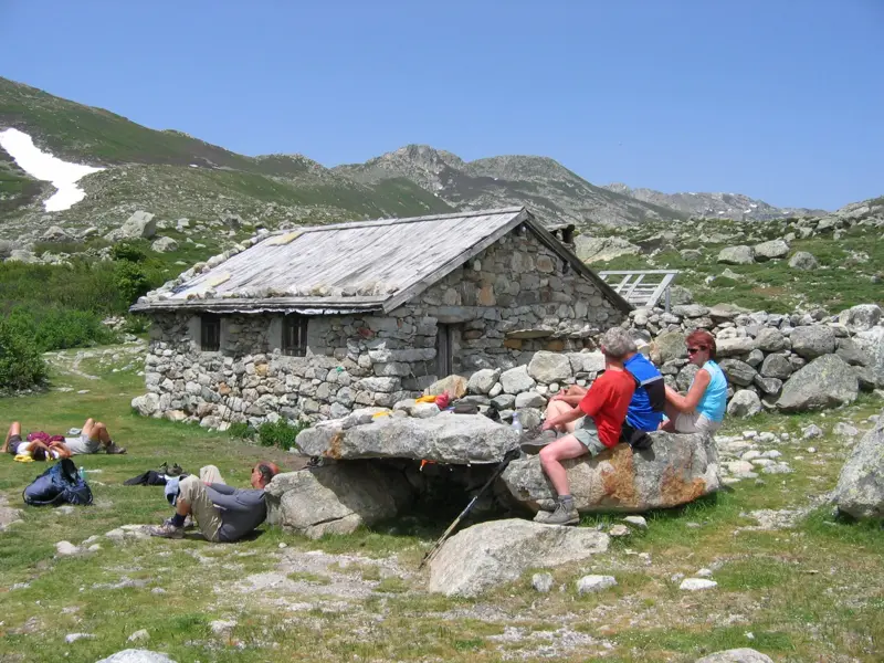 Wanderer entspannen bei einer Rast an einer rustikalen Schäferei während des GR20-Trekkings auf Korsika.