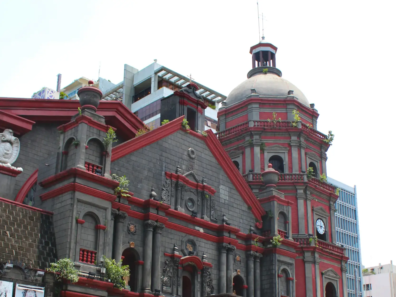 Fassade der historischen Binondo-Kirche in Manila mit rotem Zierrat und Glockenturm vor einem modernen Hochhaus im Hintergrund.