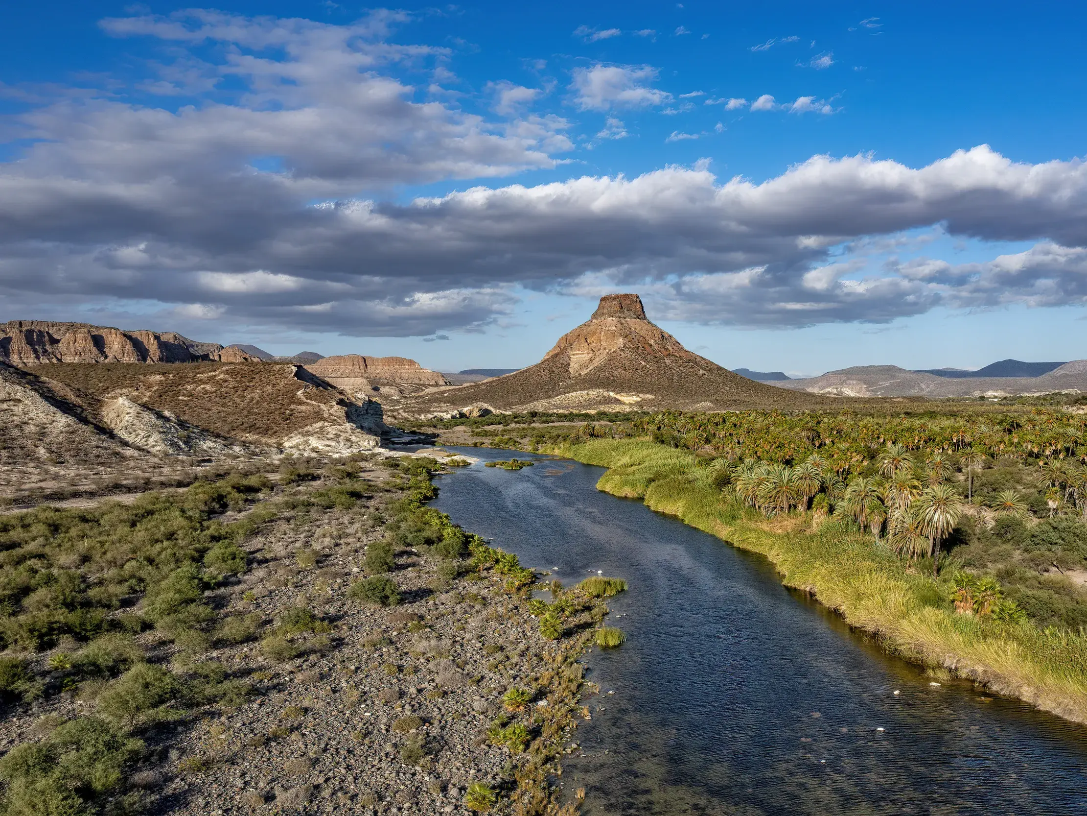 Weite Landschaft der Oase La Purísima auf der Baja California mit Fluss, Palmen und dem markanten Cerro El Pilón.