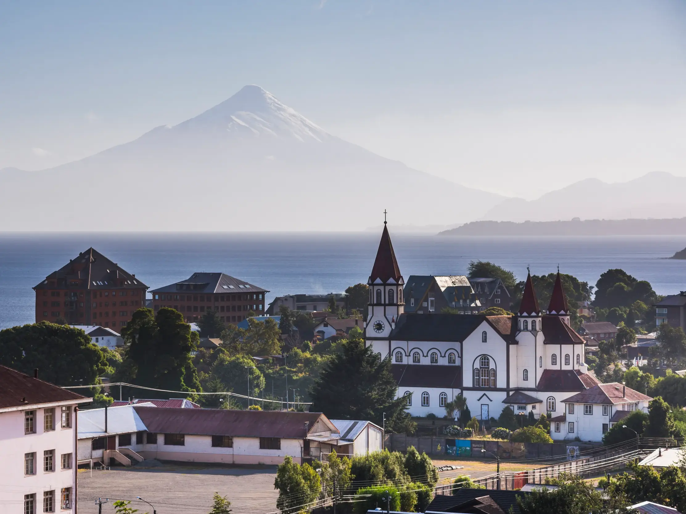 Blick über die Dächer von Puerto Varas und den Llanquihue-See zum schneebedeckten Vulkankegel des Osorno in Chile.
