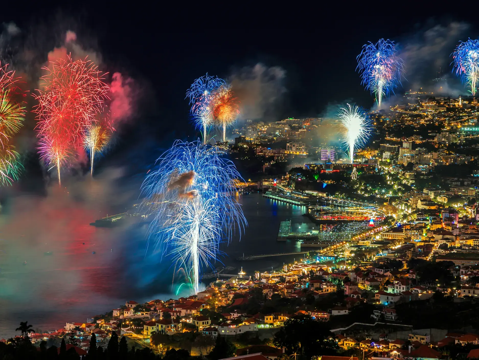 Farbenprächtiges Silvesterfeuerwerk erleuchtet den nächtlichen Himmel über der hell erleuchteten Bucht von Funchal auf Madeira.