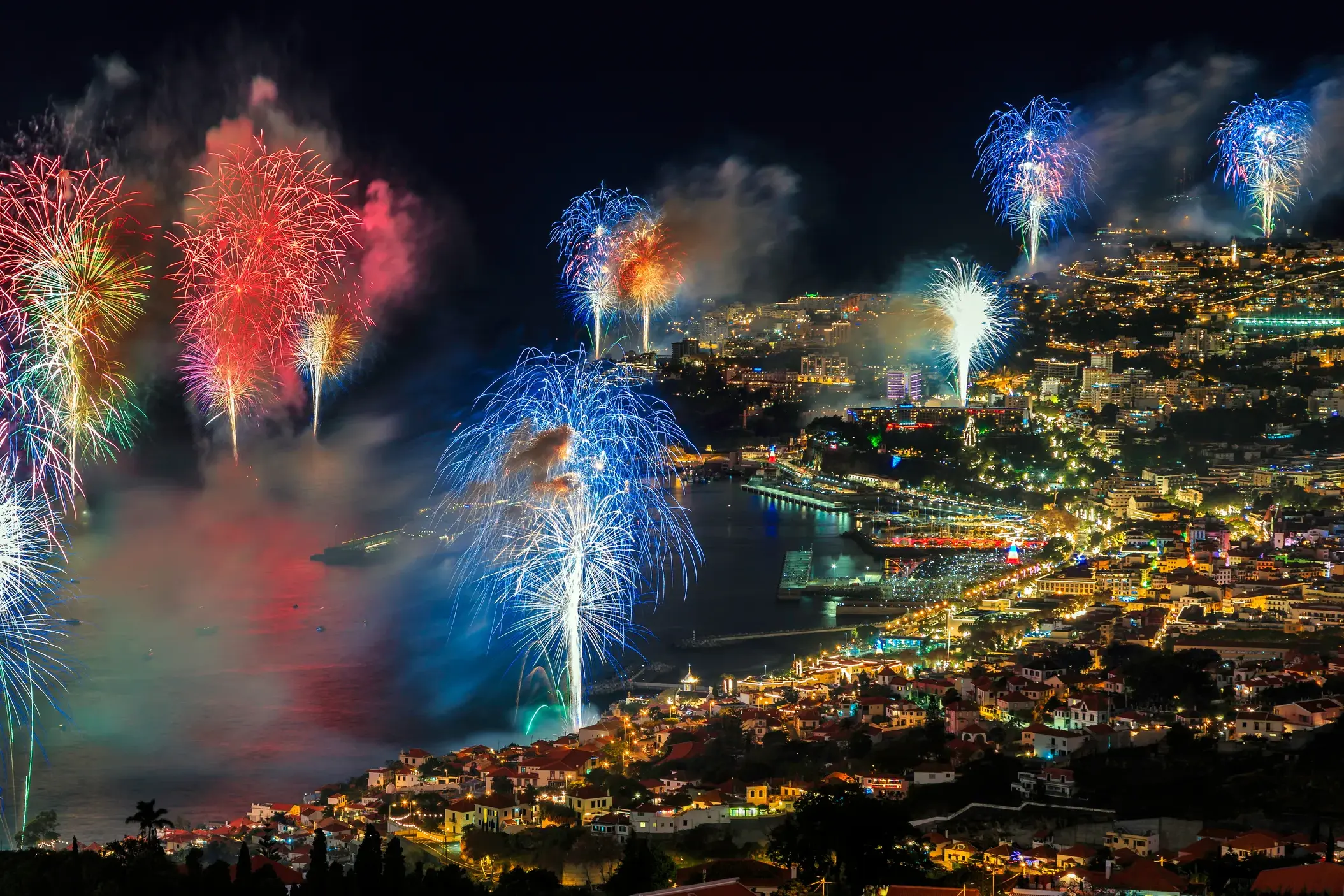 Farbenprächtiges Silvesterfeuerwerk erleuchtet den nächtlichen Himmel über der hell erleuchteten Bucht von Funchal auf Madeira.