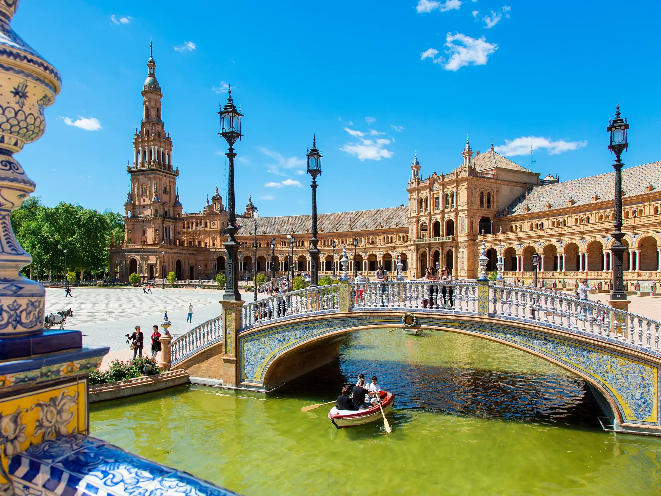 Der sonnige Plaza de España in Sevilla mit verzierter Brücke, Kanal und einem Ruderboot vor dem Hauptgebäude.