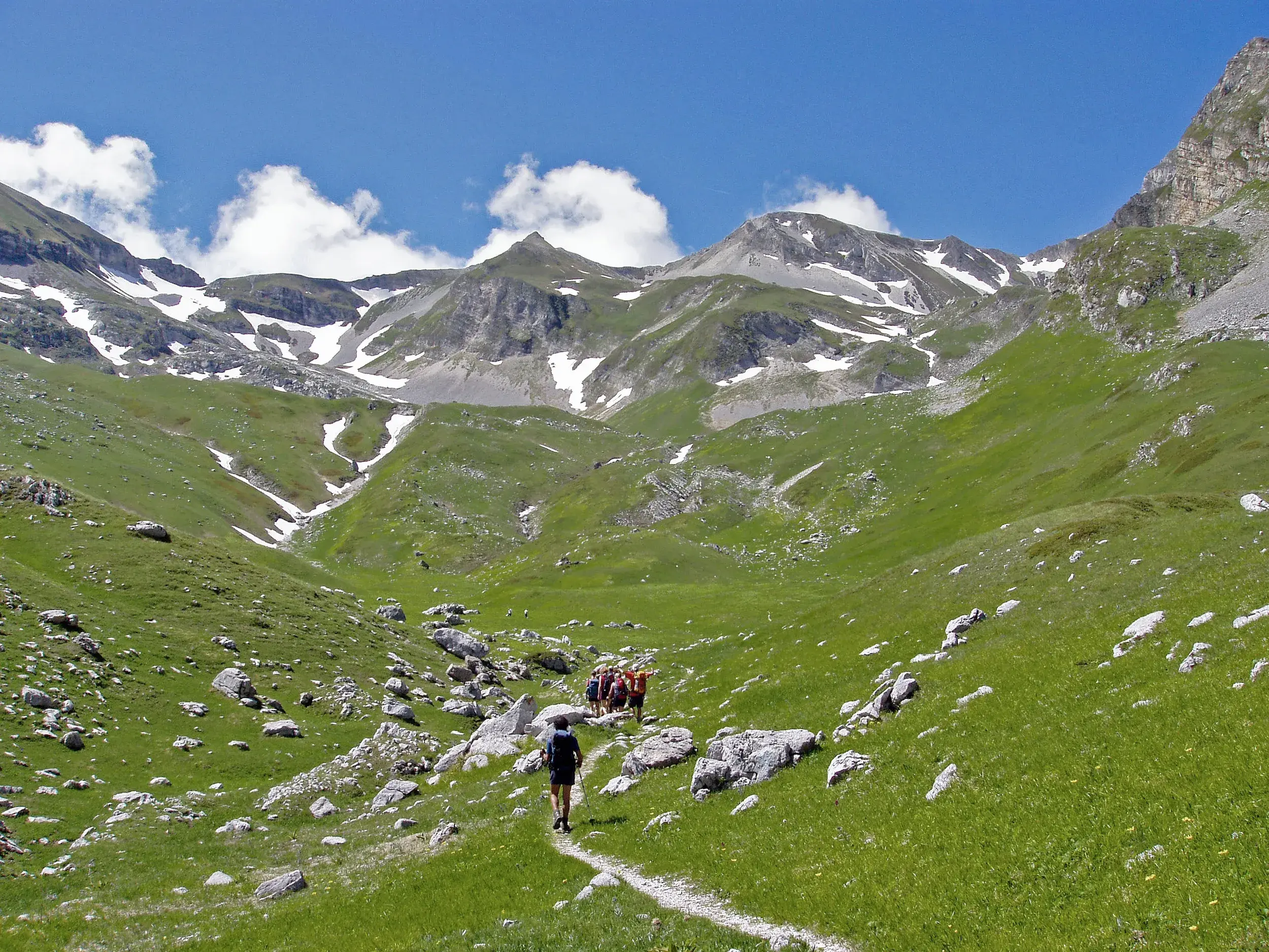 Eine Trekkinggruppe wandert auf einem schmalen Pfad durch die grüne Bergwelt des Nationalparks Gran Sasso in den Abruzzen.