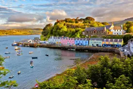 Bunte Häuserzeile am malerischen Hafen von Portree auf der Hebrideninsel Skye, mit Booten in der Bucht bei Abendsonne.
