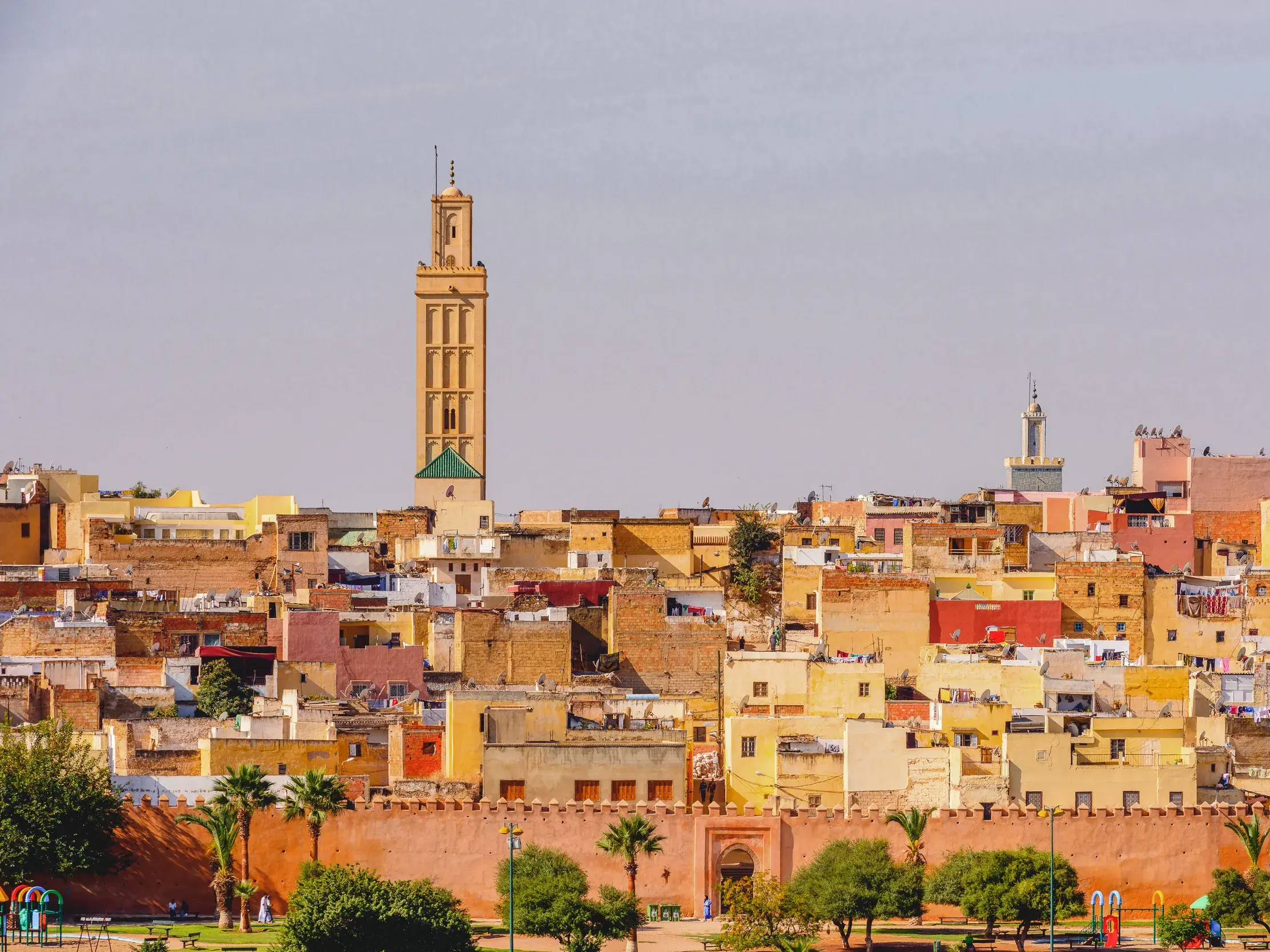 Weitblick auf die historische Medina von Marrakesch mit ihren farbenfrohen Häusern, Palmen und einem hohen Minarett bei Tag.