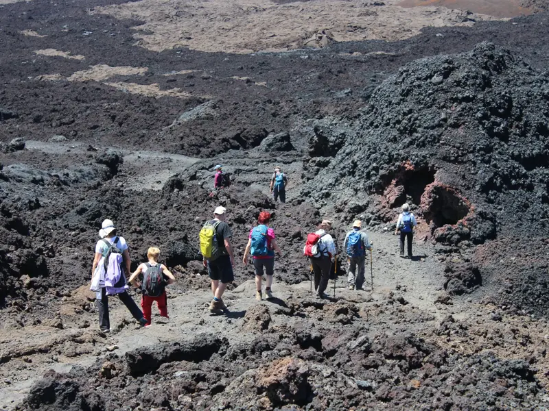Eine Wandergruppe mit Rucksäcken beim Trekking durch die karge Vulkanlandschaft des Piton de la Fournaise auf La Réunion.