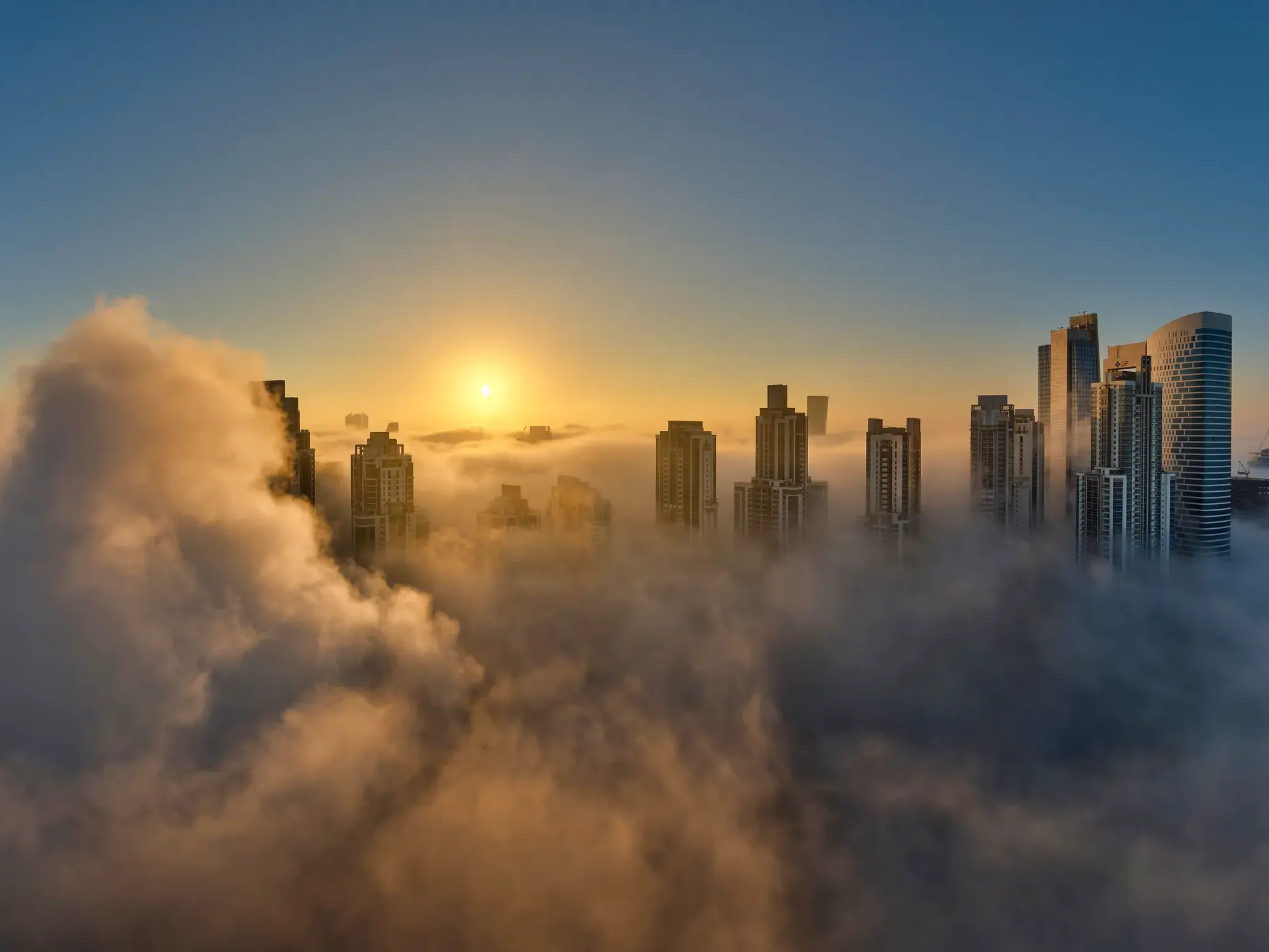 Die Skyline von Dubai mit dem Burj Khalifa und weiteren Wolkenkratzern, die bei Sonnenaufgang aus einer dichten Nebeldecke ragen.