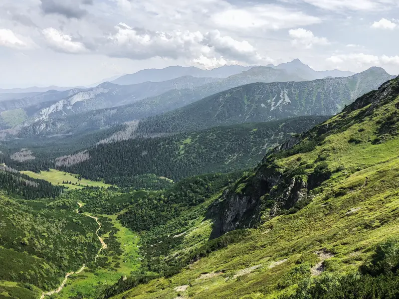 Panoramablick während einer Wanderung in der Hohen Tatra über ein grünes Tal mit Wanderweg und ferne Bergketten.