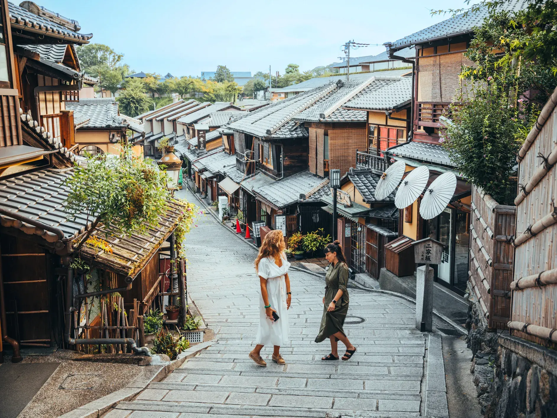 Zwei Alleinreisende erkunden die traditionellen Holzhäuser und Steinstufen im malerischen Gion-Viertel in Kyoto.