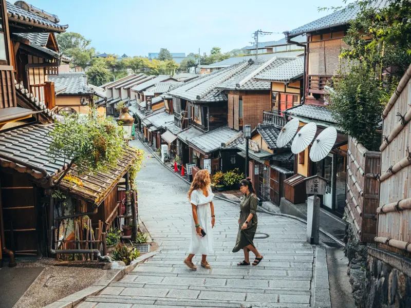 Zwei Alleinreisende erkunden die traditionellen Holzhäuser und Steinstufen im malerischen Gion-Viertel in Kyoto.