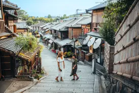 Zwei Alleinreisende erkunden die traditionellen Holzhäuser und Steinstufen im malerischen Gion-Viertel in Kyoto.