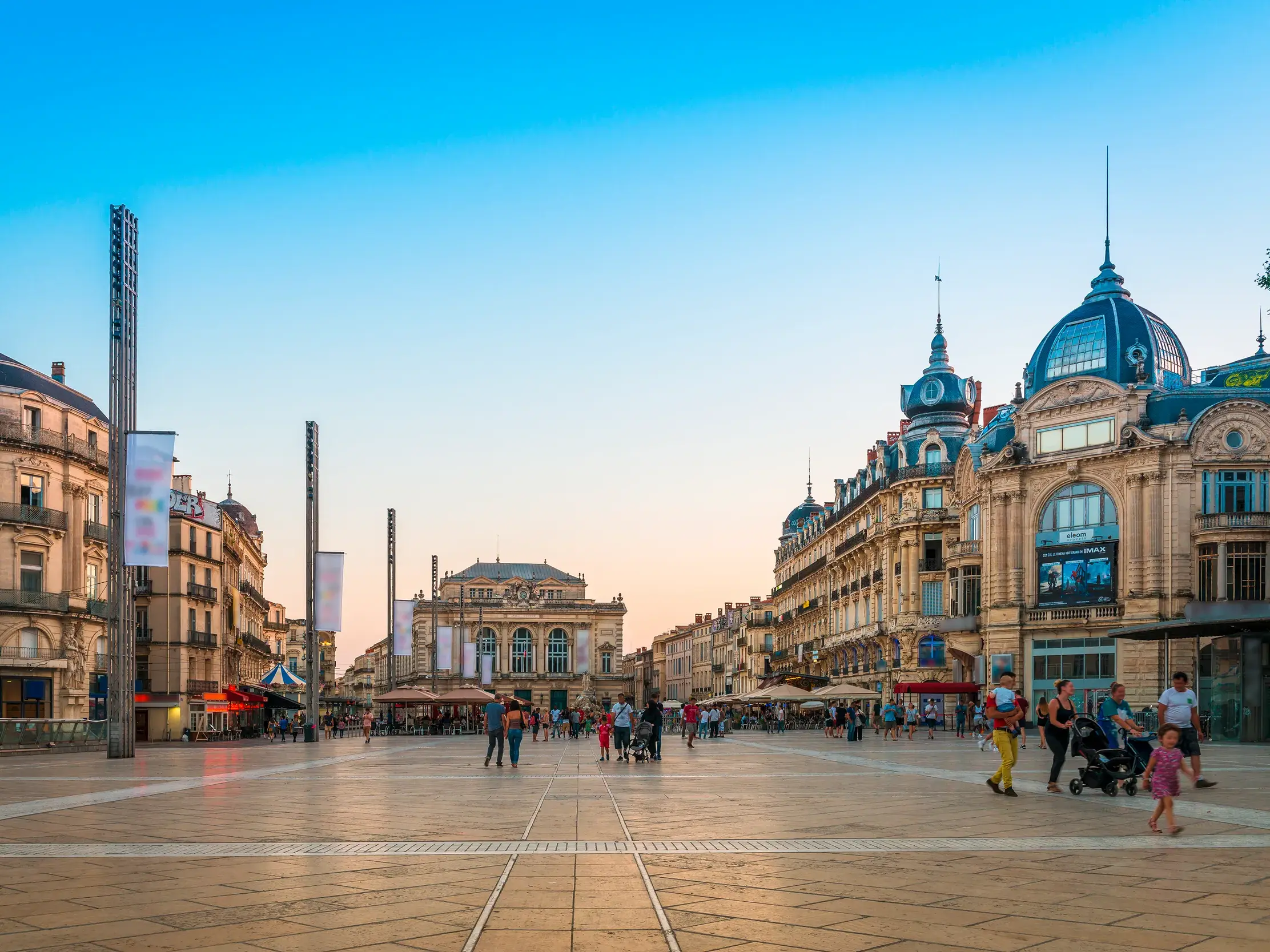 Der belebte Place de la Comédie in Montpellier im sanften Abendlicht, flankiert von historischen Gebäuden und dem Opernhaus.