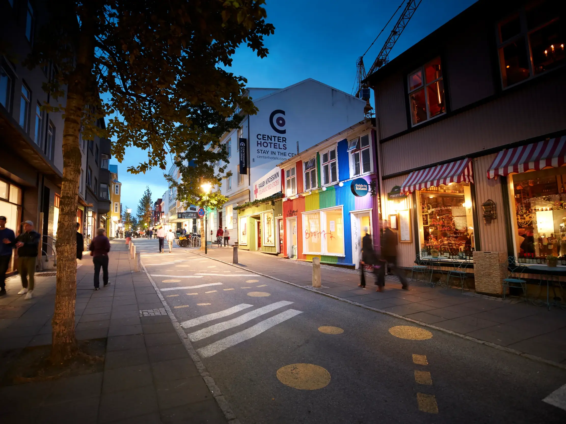 Flanierende Passanten auf der Einkaufsstraße Laugavegur in Reykjavik bei Dämmerung mit bunt bemalten, beleuchteten Häusern.