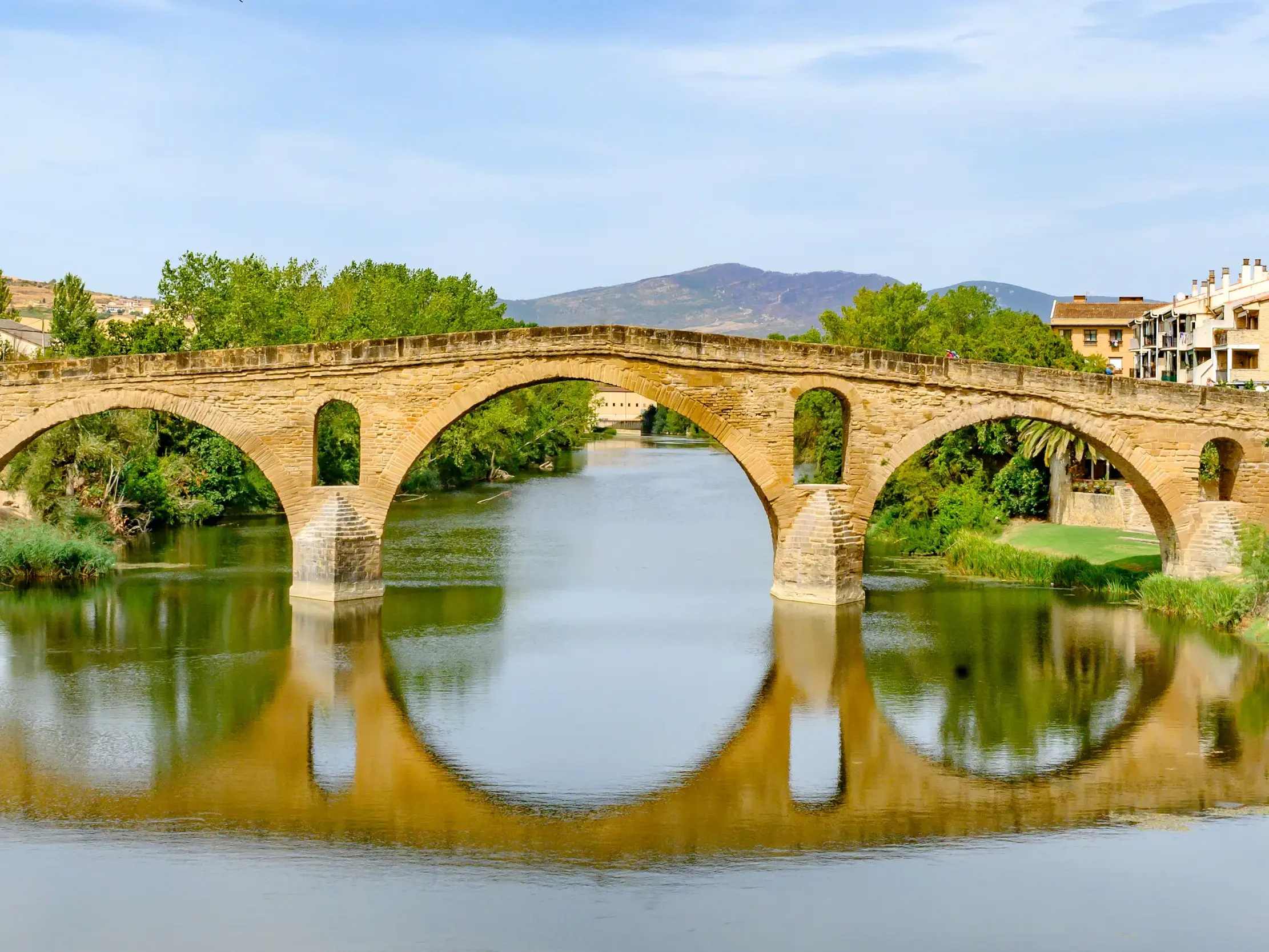 Die romanische Pilgerbrücke von Puente la Reina am Jakobsweg spiegelt sich mit ihren Bögen im ruhigen Fluss Arga.