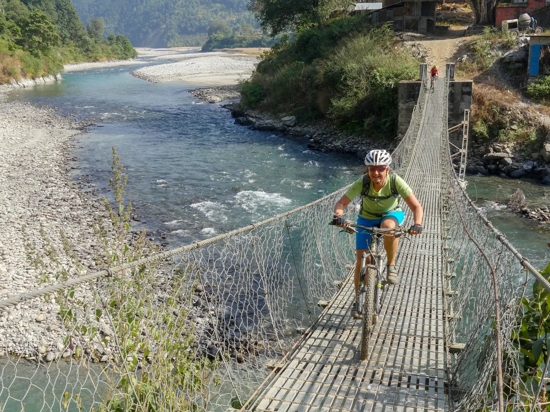 Ein Radfahrer überquert auf einer Mountainbike-Reise in Nepal eine schmale Hängebrücke über einen wilden Gebirgsfluss.