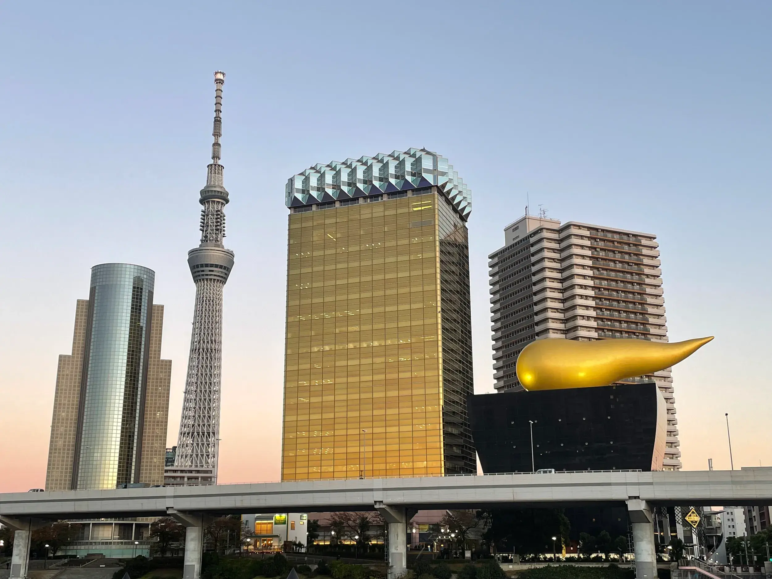 Die moderne Skyline von Tokyo im Abendlicht mit dem Tokyo Skytree und der goldenen Flamme der Asahi Beer Hall am Sumida-Fluss.