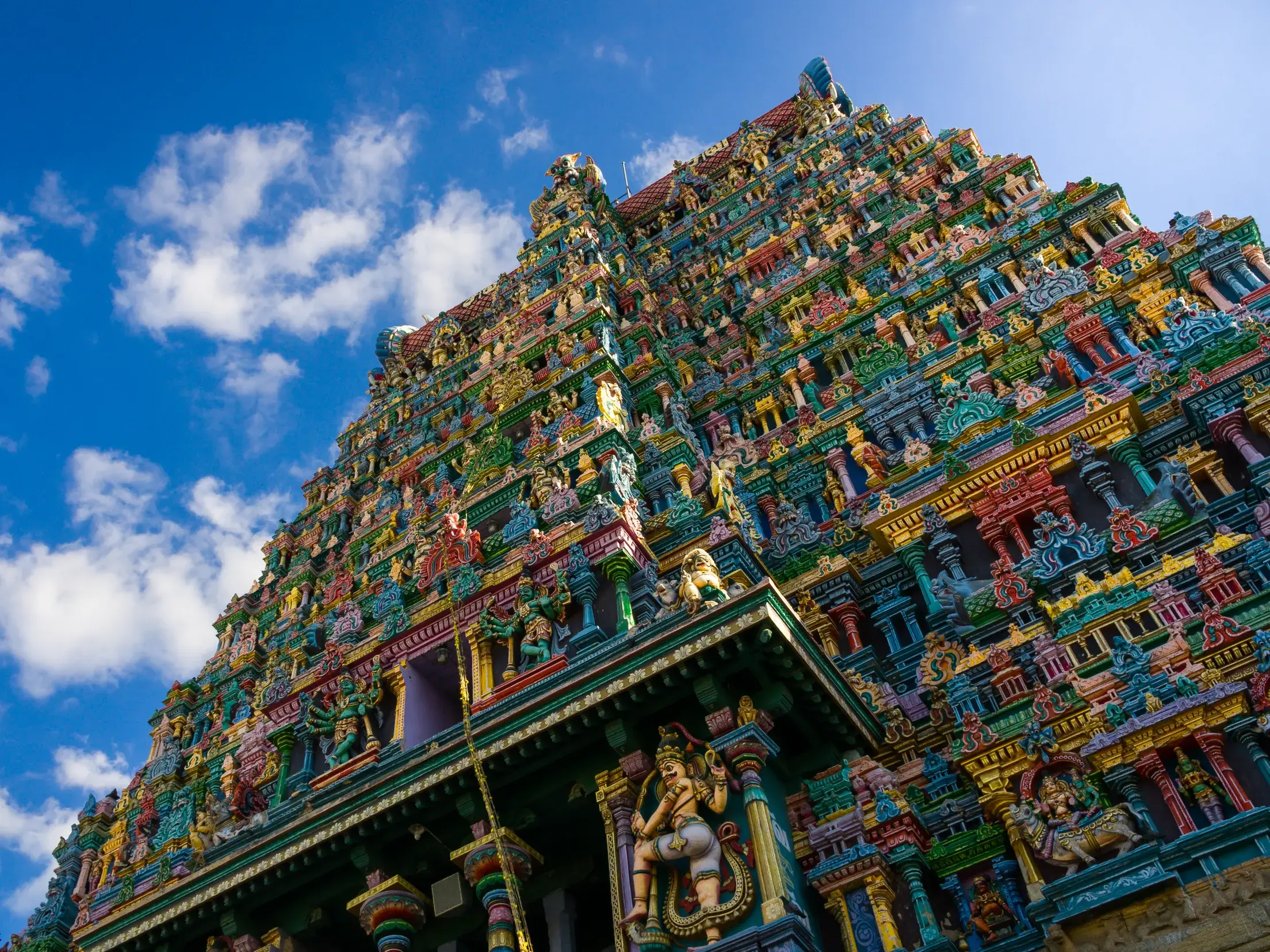 Farbenprächtiger, mit unzähligen Götterfiguren verzierter Gopuram des Meenakshi-Tempels in Madurai vor blauem Himmel.