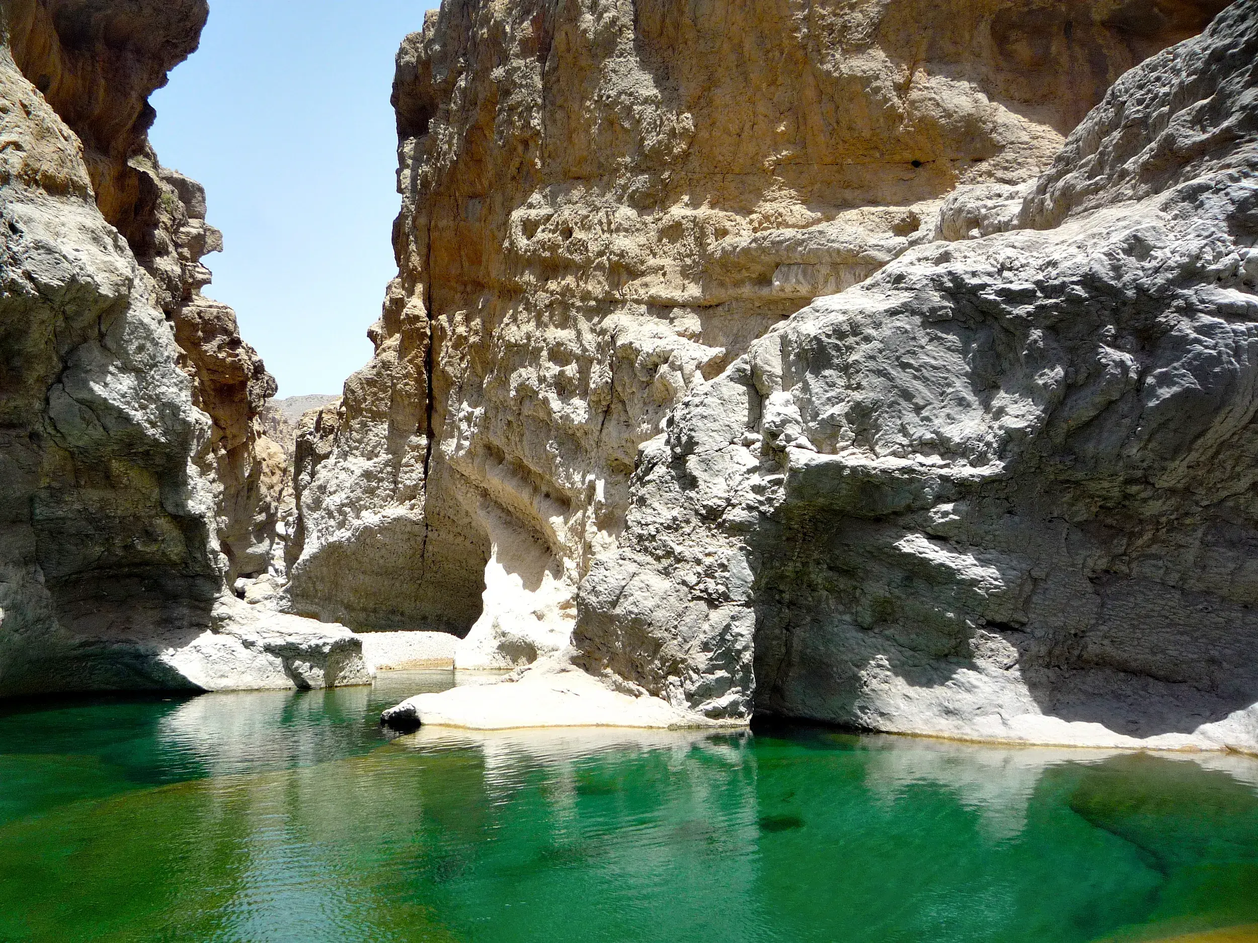 Smaragdgrünes Wasser eines Naturpools zwischen hohen Felswänden im Wadi Bani Khalid lädt zur Abkühlung auf einer Trekkingreise ein.