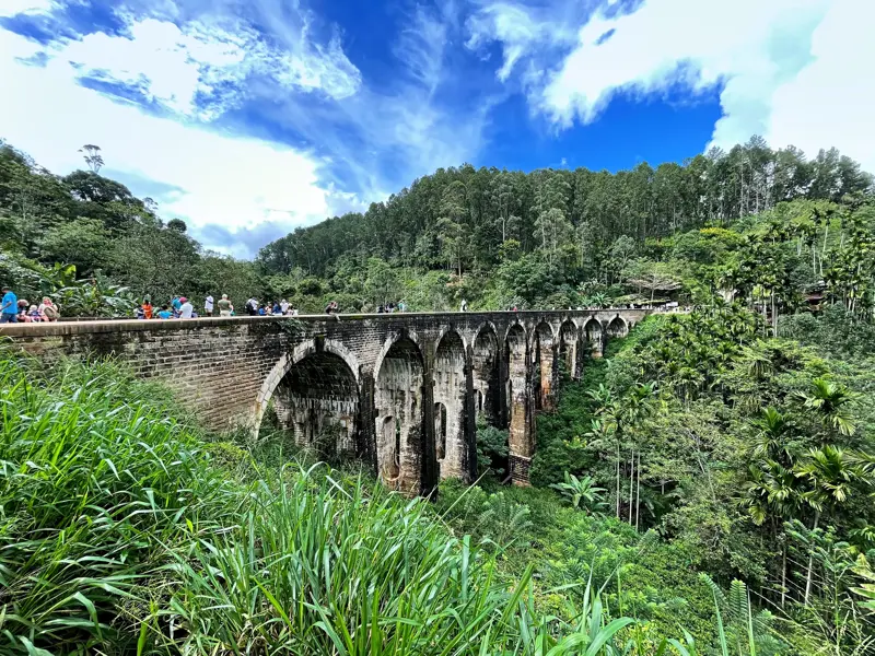 Eine Reisegruppe spaziert über die imposante Nine Arches Bridge, ein Steinviadukt im grünen Hochland von Ella, Sri Lanka.