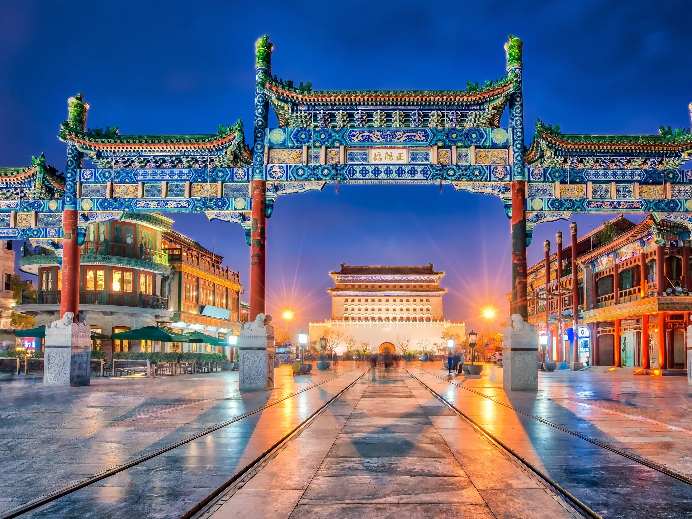 Farbenfrohes Paifang-Tor auf der beleuchteten Qianmen-Straße in Beijing bei Nacht. Im Hintergrund ist das Zhengyangmen-Tor zu sehen.