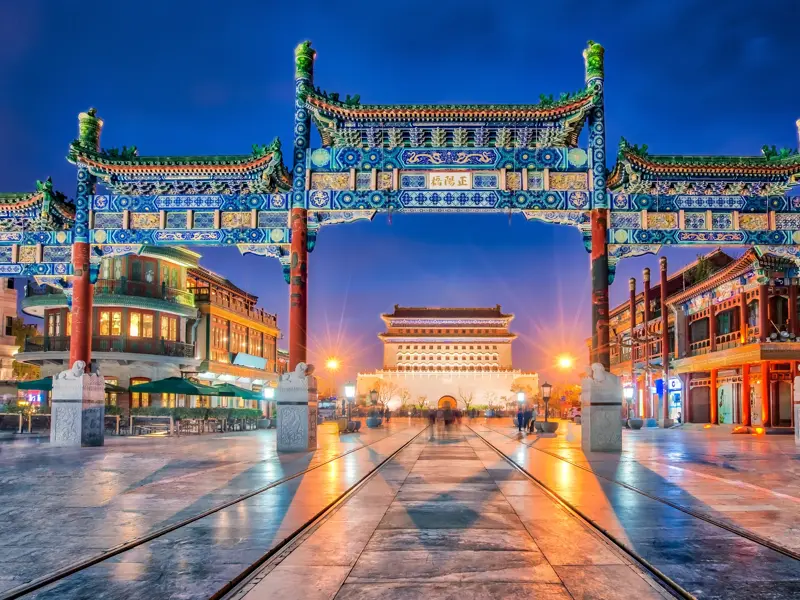 Farbenfrohes Paifang-Tor auf der beleuchteten Qianmen-Straße in Beijing bei Nacht. Im Hintergrund ist das Zhengyangmen-Tor zu sehen.
