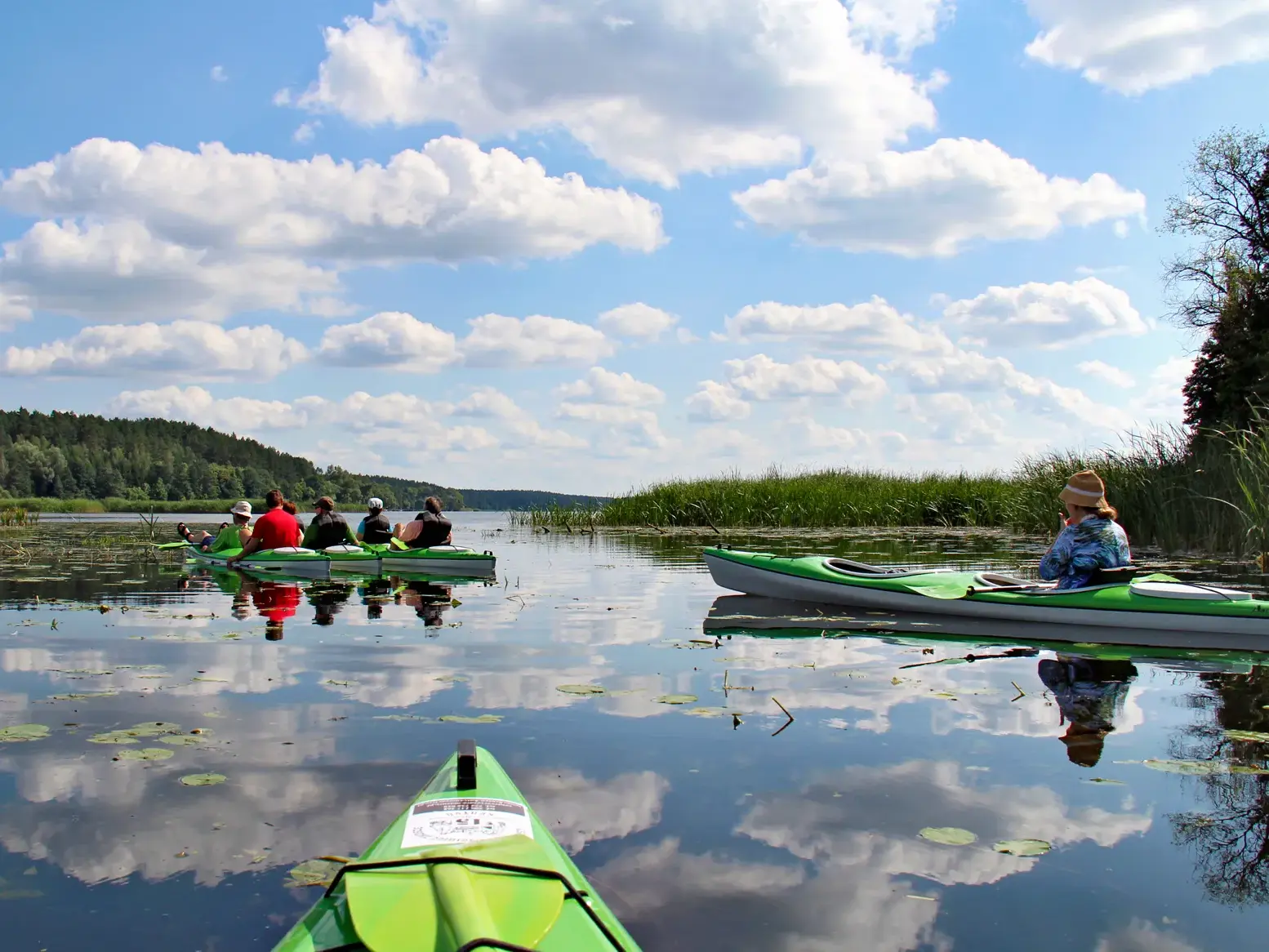 Hauser-Reisegruppe bei einer Kajaktour auf der Krutynia, der Himmel mit Wolken spiegelt sich im ruhigen Wasser.