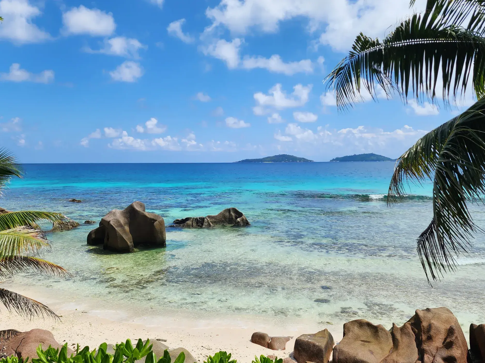 Weiße Sandbucht mit Granitfelsen am türkisfarbenen Indischen Ozean, im Hintergrund Inseln der Seychellen.