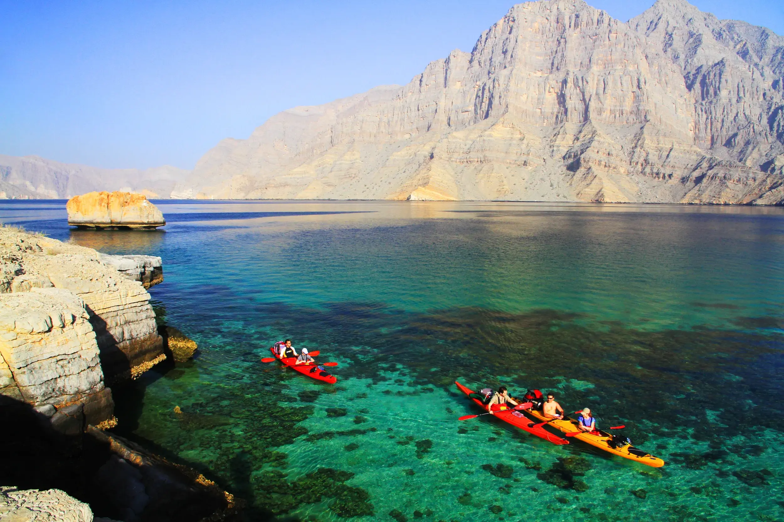 Reisegruppe beim Kajak-Trekking im türkisen Meer vor den steilen Felsklippen der Halbinsel Musandam im Oman.