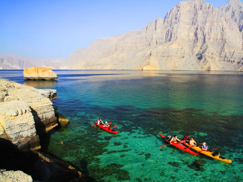 Reisegruppe beim Kajak-Trekking im türkisen Meer vor den steilen Felsklippen der Halbinsel Musandam im Oman.