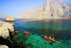 Reisegruppe beim Kajak-Trekking im türkisen Meer vor den steilen Felsklippen der Halbinsel Musandam im Oman.