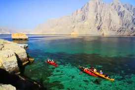 Reisegruppe beim Kajak-Trekking im türkisen Meer vor den steilen Felsklippen der Halbinsel Musandam im Oman.