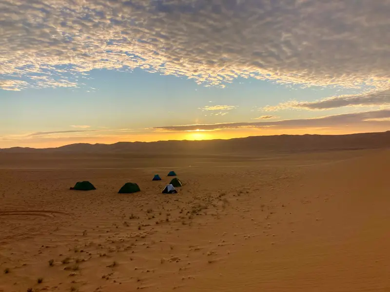 Zeltlager einer Hauser-Trekkinggruppe bei Sonnenuntergang in der weiten Dünenlandschaft des Tassili n'Ajjer Nationalparks.