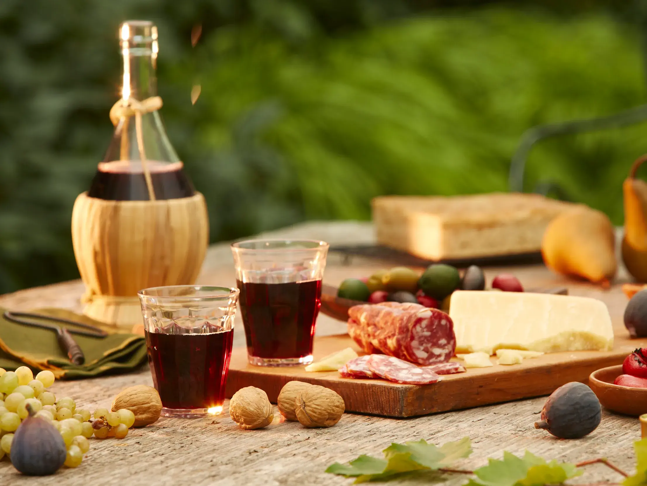 Rustikaler Holztisch mit toskanischen Spezialitäten: Chianti-Wein, Pecorino-Käse, Salami, Feigen und Walnüssen im Grünen.