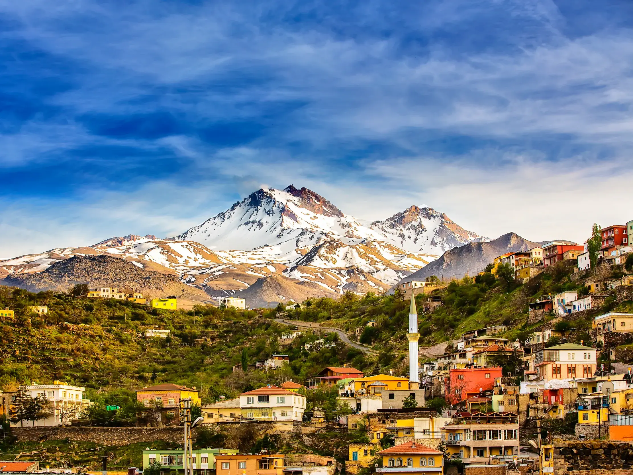 Blick auf ein farbenfrohes Dorf mit einem Minarett an den Hängen des schneebedeckten Berges Erciyes in der Nähe von Kayseri