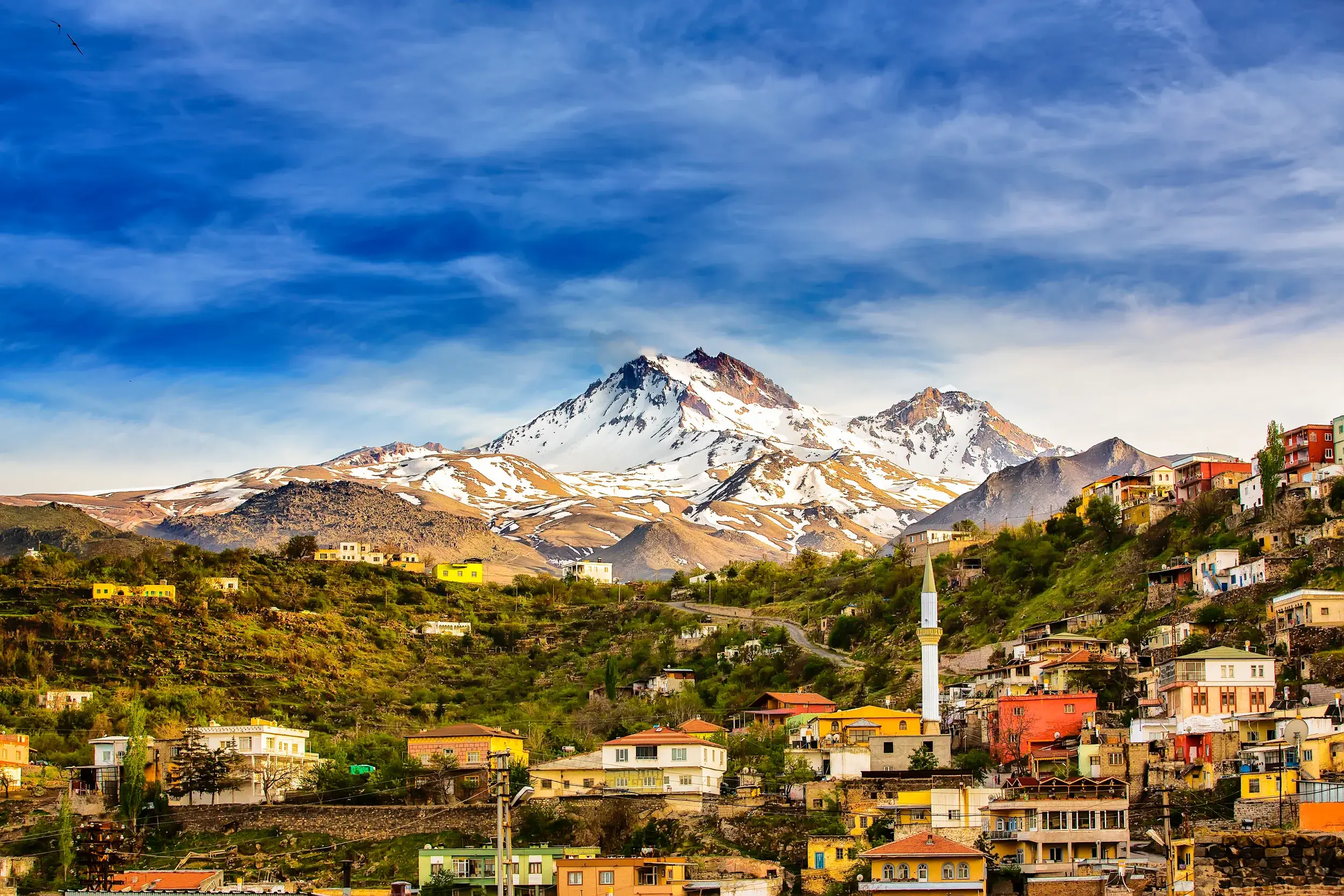 Blick auf ein farbenfrohes Dorf mit einem Minarett an den Hängen des schneebedeckten Berges Erciyes in der Nähe von Kayseri