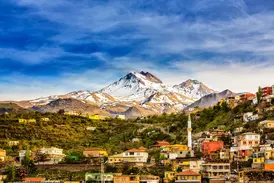Blick auf ein farbenfrohes Dorf mit einem Minarett an den Hängen des schneebedeckten Berges Erciyes in der Nähe von Kayseri